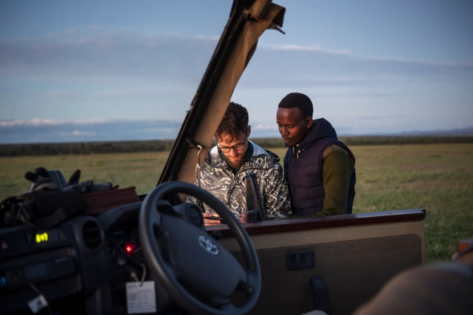 En guide och en gäst går igenom dagens tur vid ratten i en öppen safaribil i kvällsljus