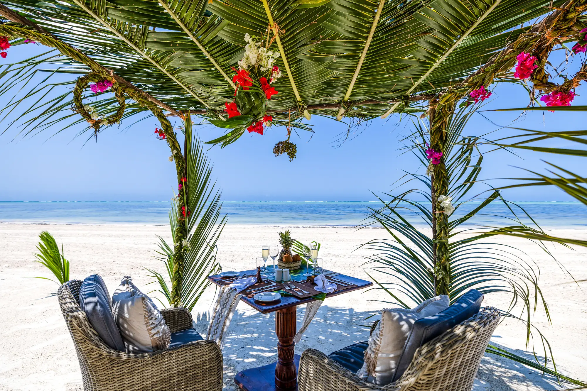 Dukat bord för två under blomstersmyckad paviljong på stranden vid The Palms